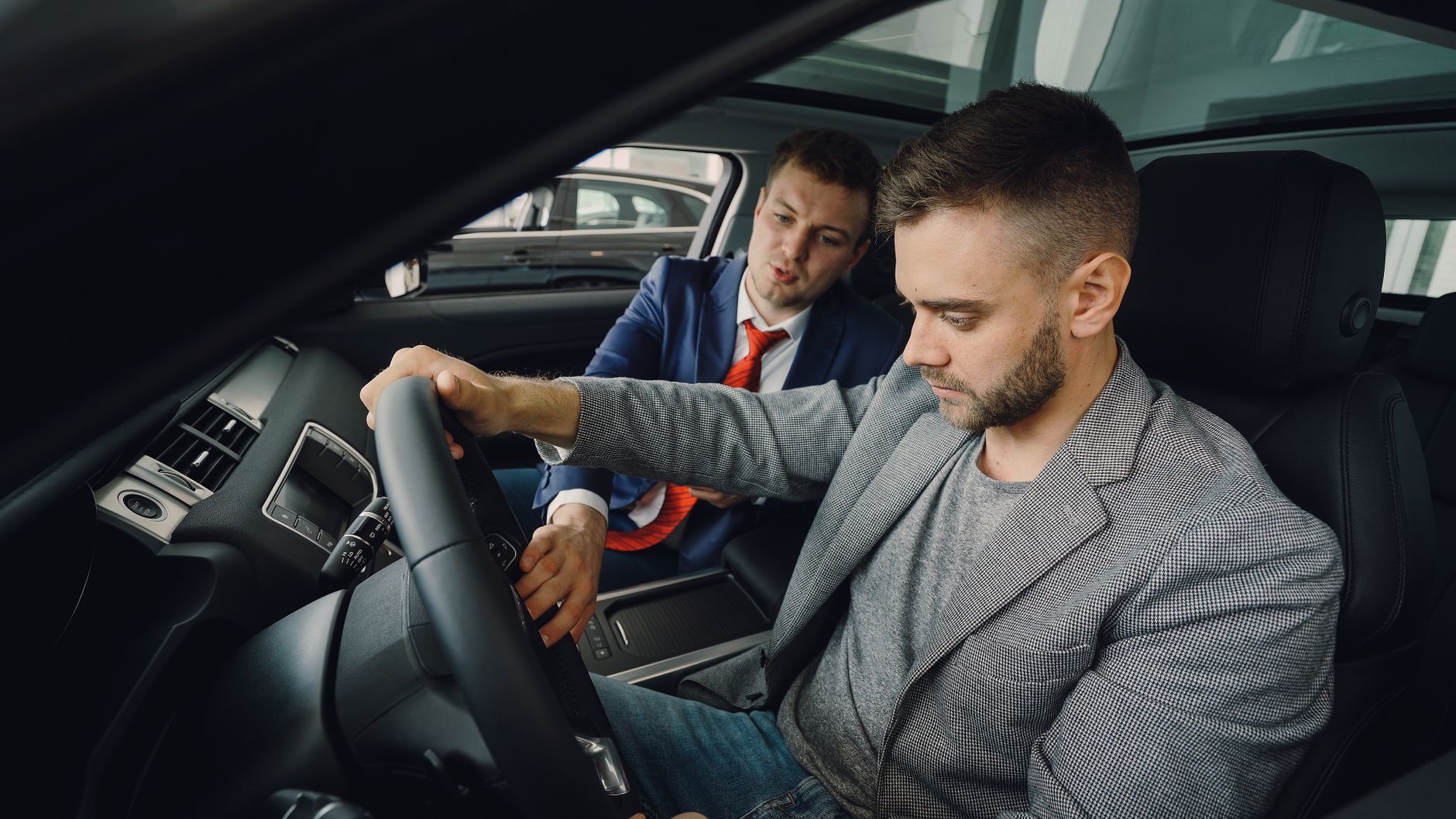 Car salesman showing buyer vehicle features and unsigned title document during dealership consultation inside car