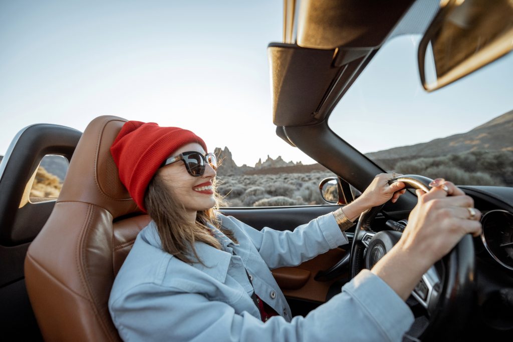 Happy woman driving convertible car on scenic road trip