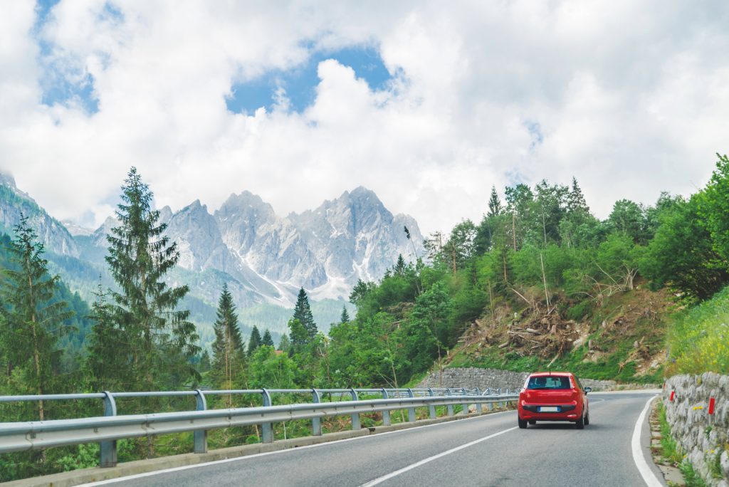 Red car driving on mountain highway through alpine forest landscape