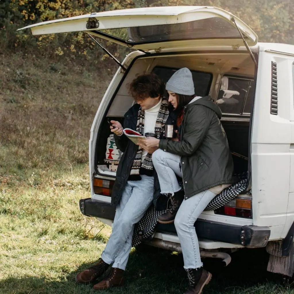 A young couple sits in the open back of a camper van reviewing a map, highlighting the importance of proper camper van title and registration before hitting the road.