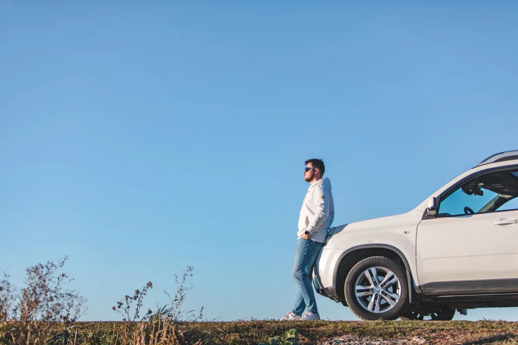 A man stands beside his white SUV under a clear blue sky, representing Montana LLC vehicle registration and formation services for out-of-state vehicle owners.