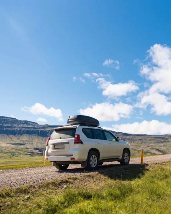 A white SUV with rooftop cargo is parked on a scenic rural road surrounded by open landscape, representing freedom of travel and compliance with vehicle registration requirements.