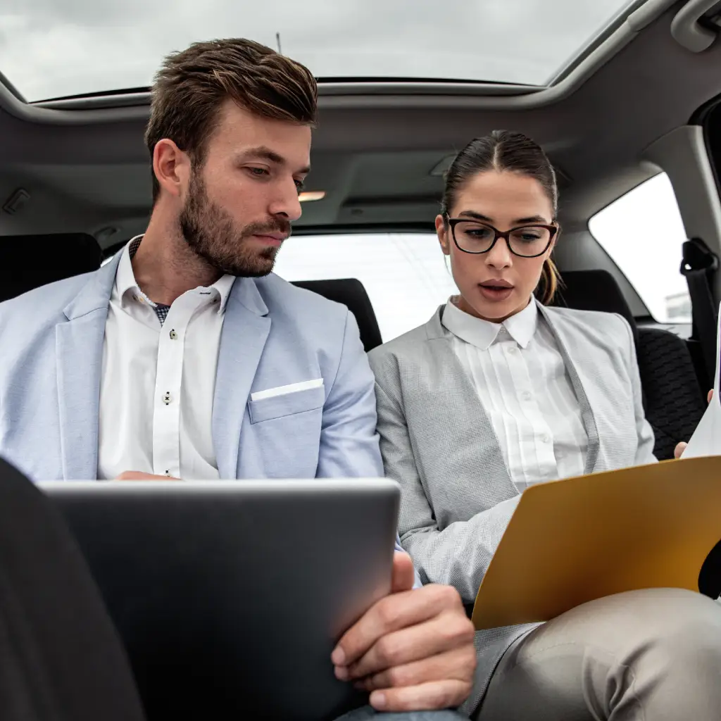 Two professionals review documents on tablets inside a vehicle, illustrating how vehicle registration LLC Montana formation enables efficient, on-the-go business decisions for registering and managing vehicles legally and seamlessly.