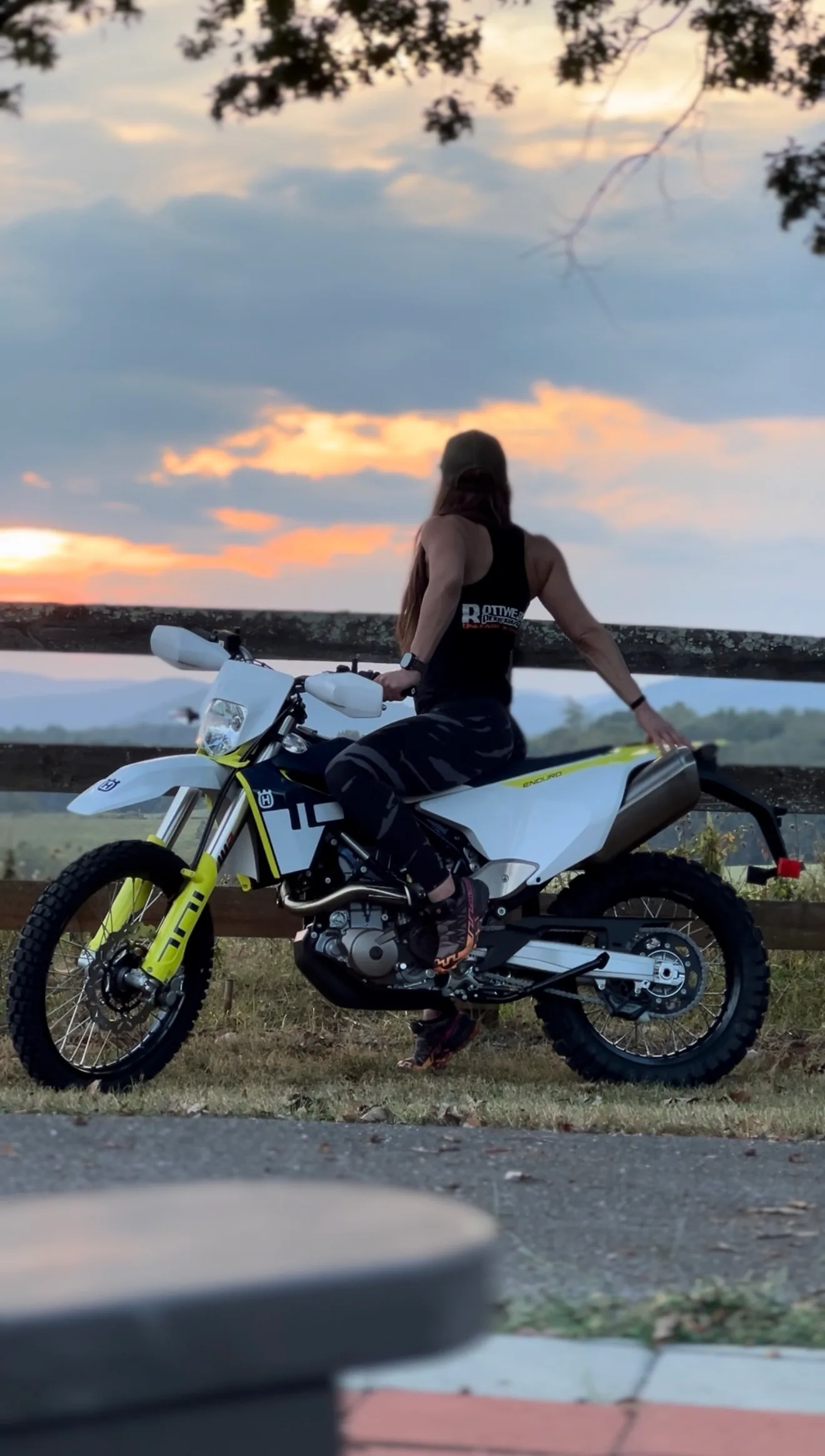 Crystalmarie looking out over a mountain range at sunset beside her Husqvarna enduro