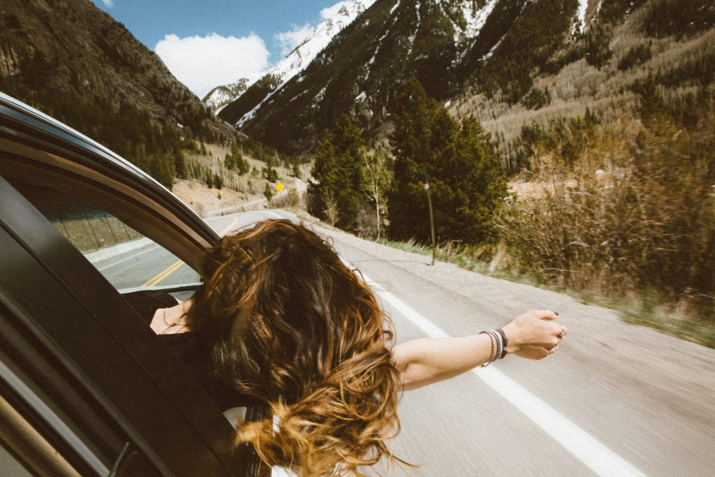 Woman leaning out car window on mountain highway, scenic road trip through forested valley landscape