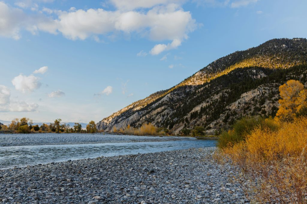 Scenic Montana landscape with river, mountains, and golden autumn trees reflecting state's natural beauty and environment.