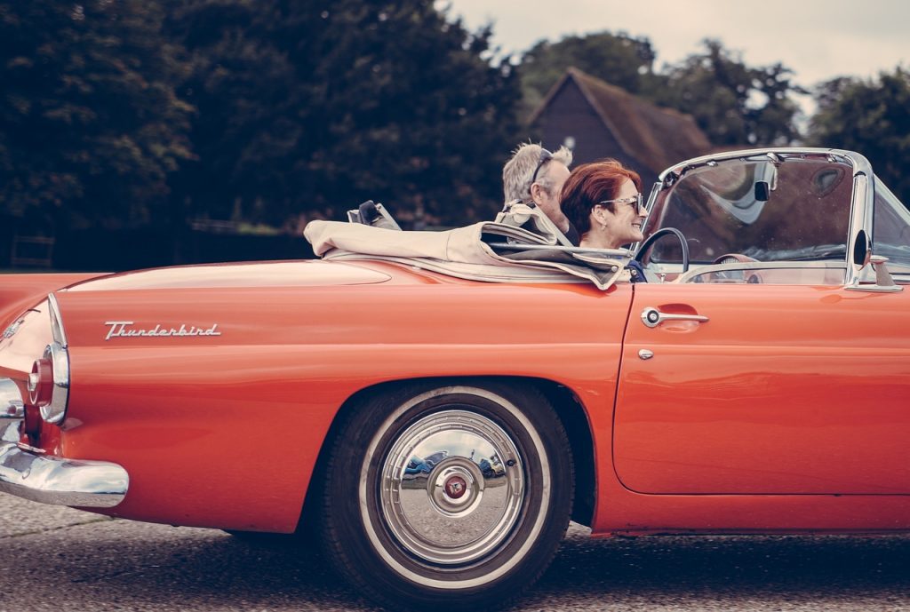 Couple driving classic red convertible Thunderbird, representing vehicle ownership and temporary registration requirements.