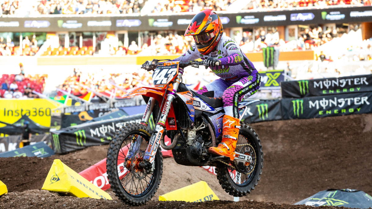 A professional motocross rider maneuvers a Dirt Legal sponsored race bike through a difficult, rutted corner section of a stadium race track.