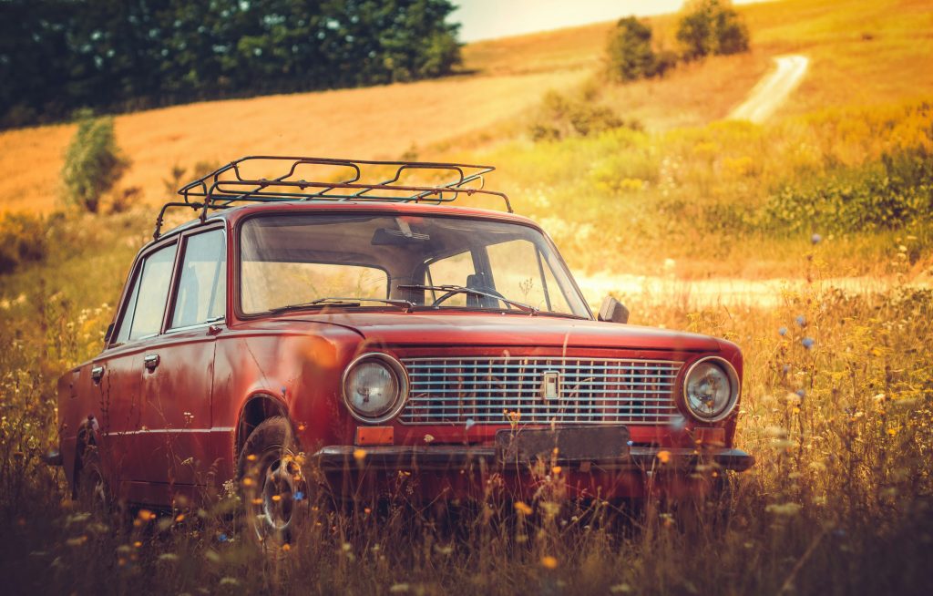 Vintage red sedan abandoned in overgrown field, illustrating salvage and rebuilt title vehicle conditions.