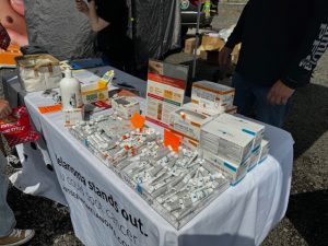 Table display with Narcan kits, medical supplies, and informational materials set up under a tent at a community outreach event.