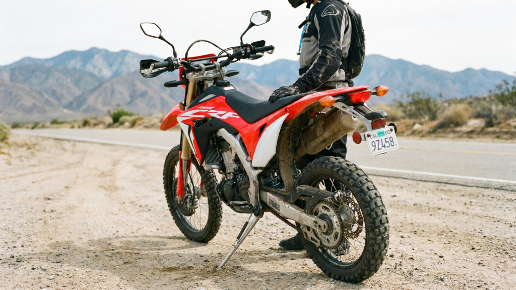 Red and white dirt bike parked on desert highway with rider in protective gear during extreme heat conditions