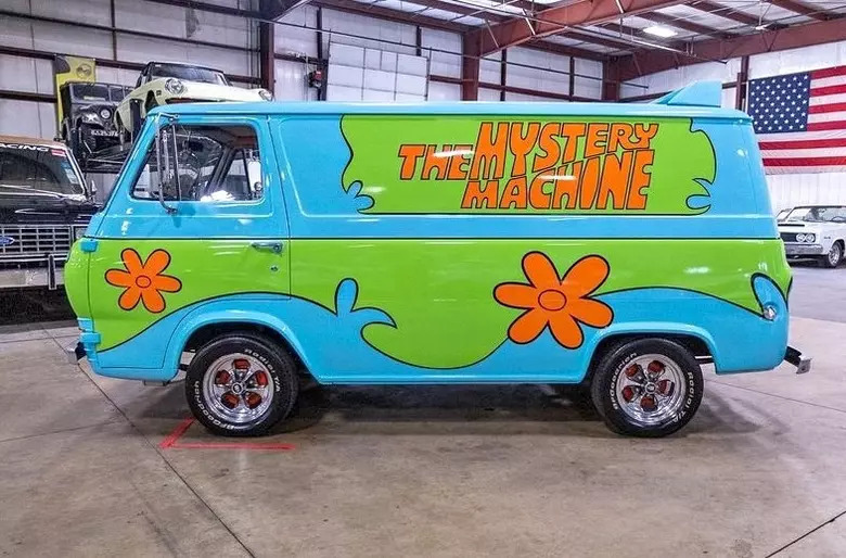 The van’s bright green and blue paint scheme, orange flower decals, and the large “The Mystery Machine” lettering on the side are all signature design elements of the iconic vehicle driven by Scooby-Doo and the Mystery Inc. gang.