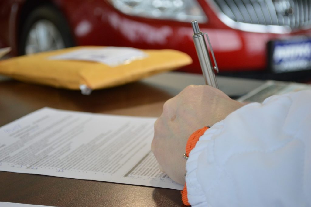 Person signing vehicle registration documents with red car in background, Montana LLC tax strategy