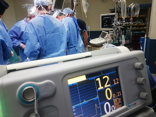 Operating room monitor displays vital signs during surgical procedure with medical team in background
