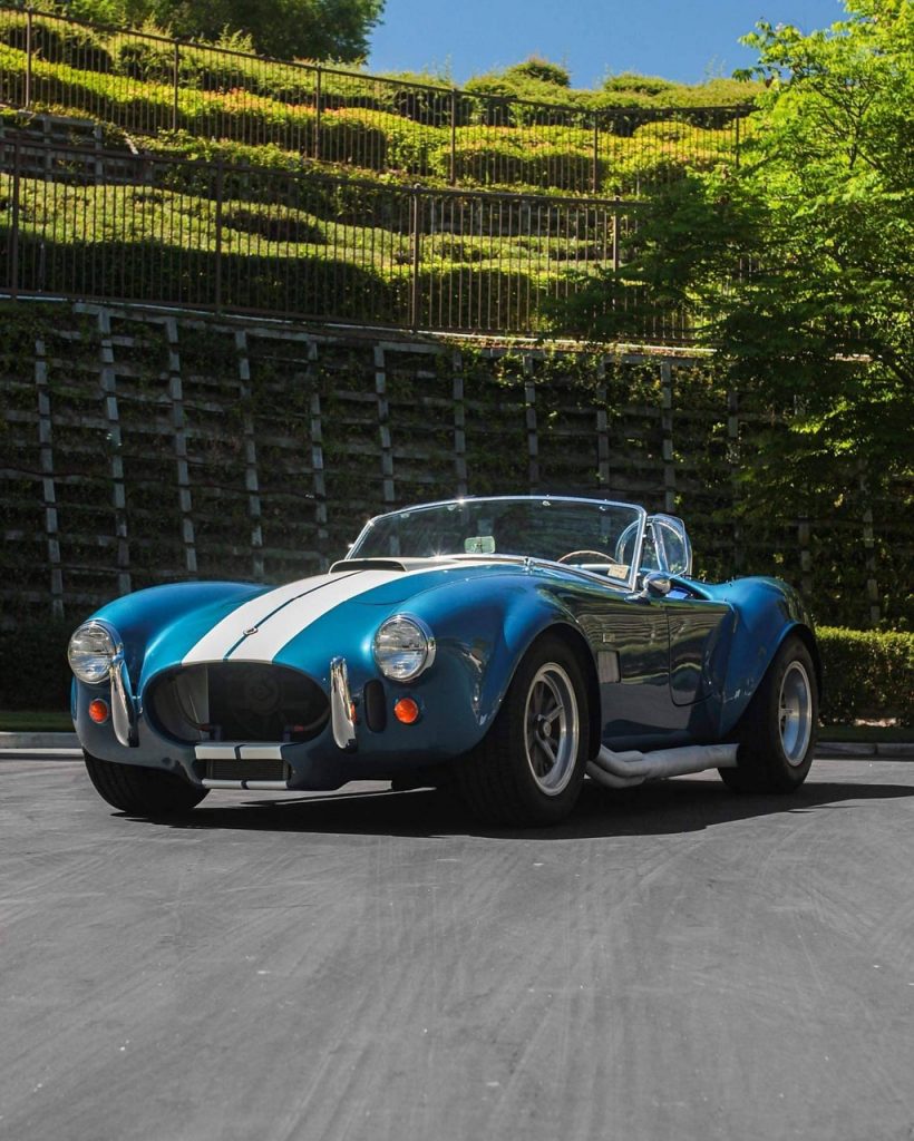 Blue and white classic Cobra race car with open door displayed in driveway, embodying legendary race car aesthetics