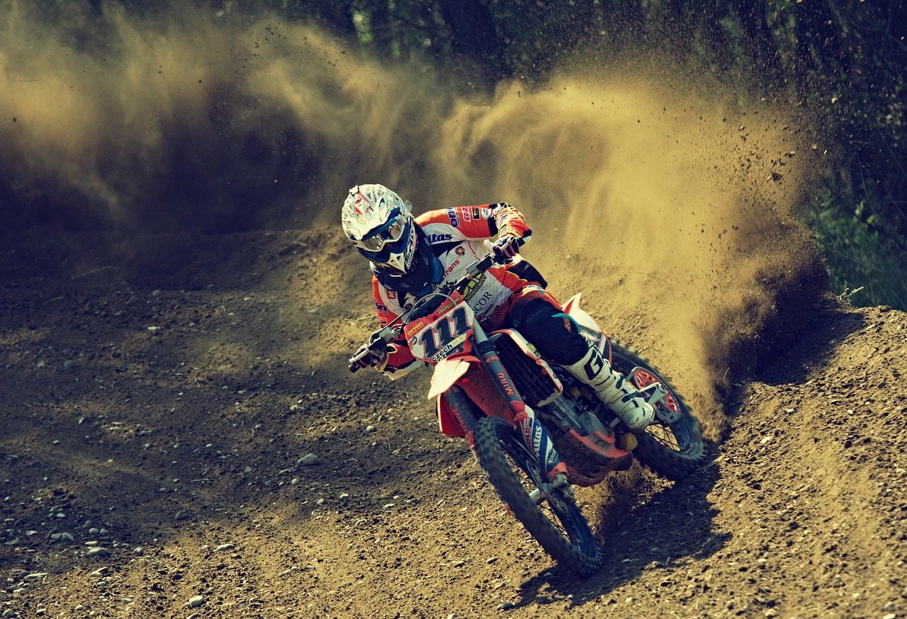 Dirt bike rider in red gear kicking up dust on off-road track during competitive motocross race event