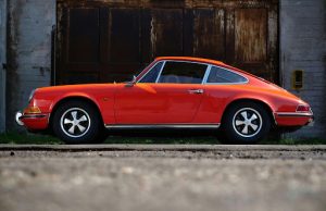 Red classic Porsche 911 sports car parked against industrial backdrop