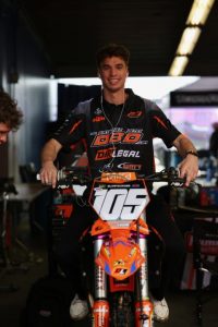 Marcus Phelps sitting on his race bike in the team pits wearing a Dirt Legal DBD Racing team shirt and headphones before the Daytona night show.