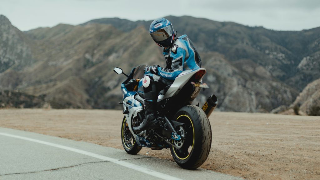 Motorcyclist in blue gear performing wheelie on desert road with mountains