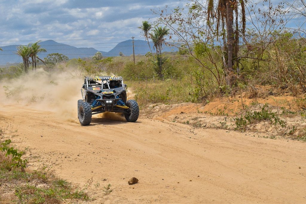 Blue and black UTV kicking up dust on sandy off-road trail through brush and trees with mountains in background