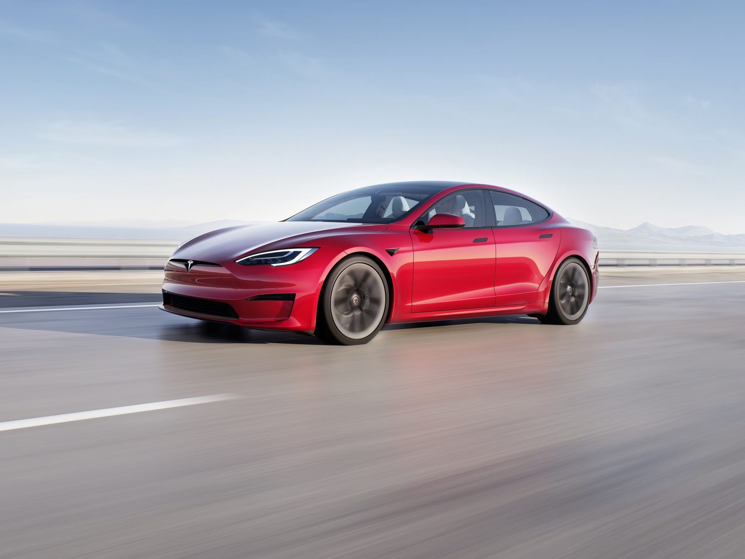 Red Tesla Model S sedan driving on highway, illustrating new vehicle purchase costs and taxes for 2025.