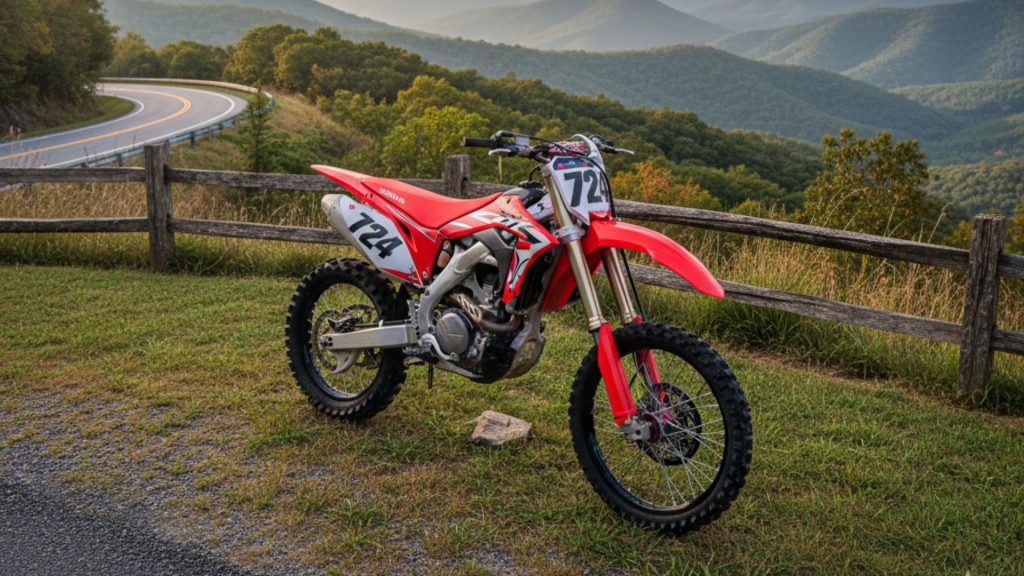 Red dirt bike parked on grass with mountain road and scenic valley view