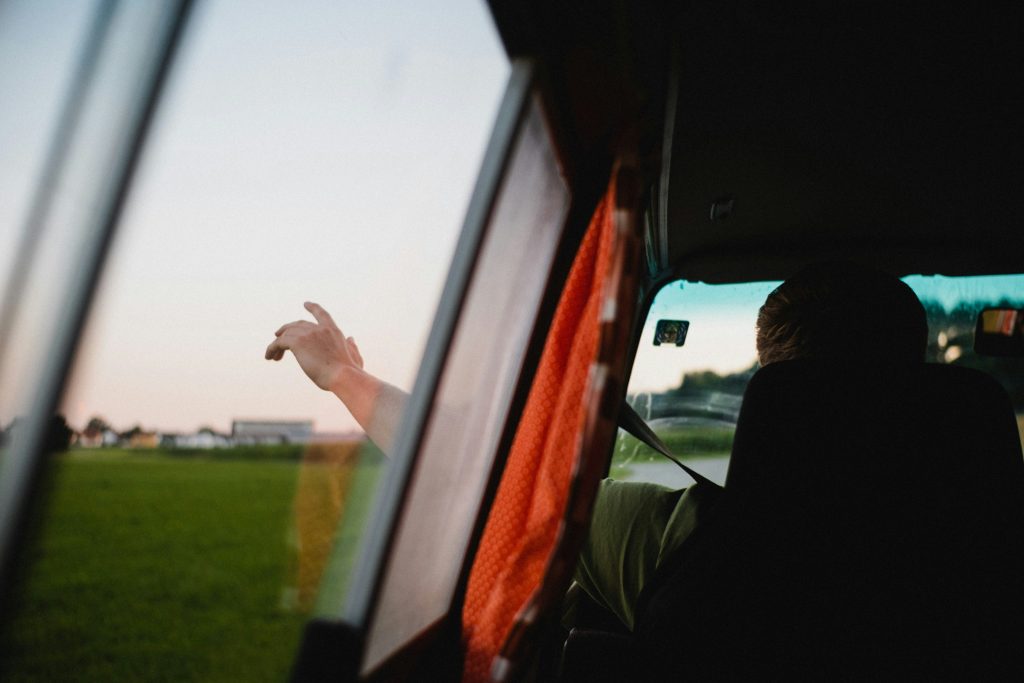 Person's hand extended from van window overlooking green fields