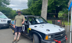 Man standing beside black and white race car promoting melanoma skin cancer awareness at motorsports event