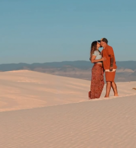 Couple in matching orange outfits embracing on sand dunes, digital nomad travel adventure lifestyle