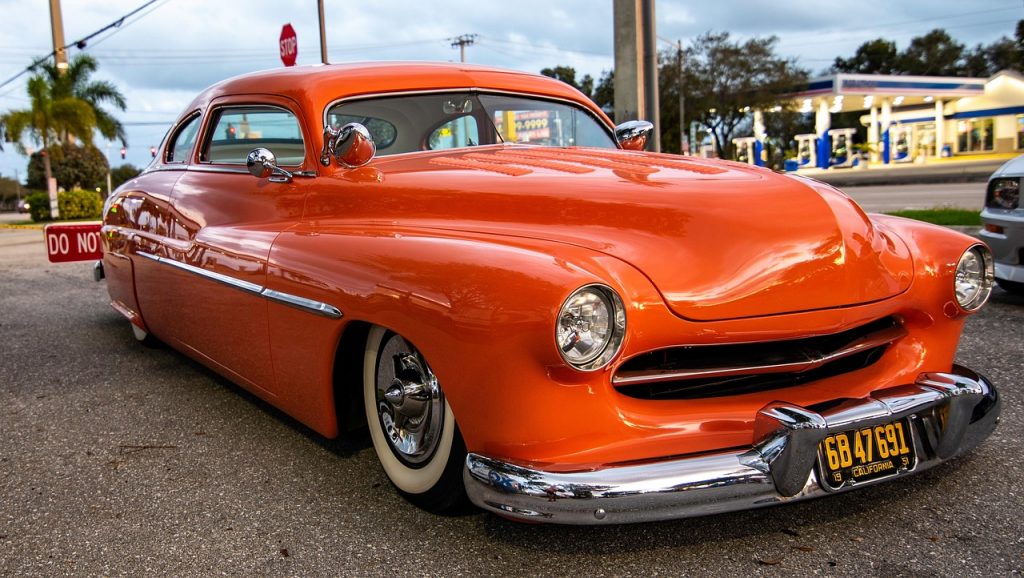 Restored vintage 1950s orange coupe with custom modifications parked on street