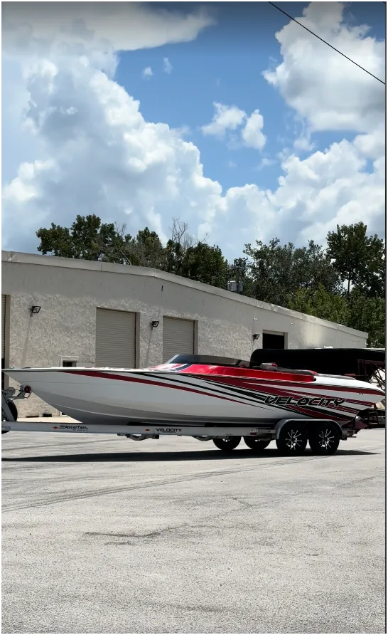 A red, white, and black Velocity VR1 Performance Sports Boat sitting on its trailer outside the Velocity facility.