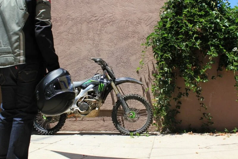 dirt bike on street and man holding helmet