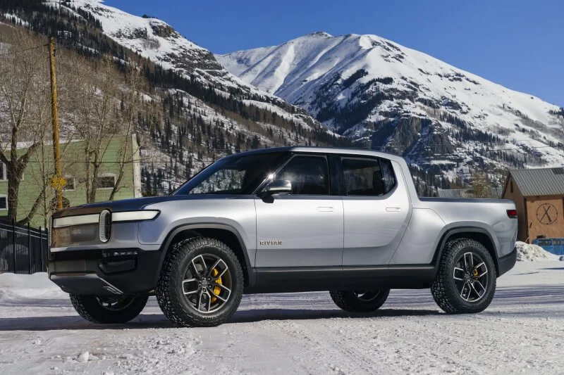 White Rivian R1T electric pickup truck parked in snowy mountain valley setting for off-road capability evaluation