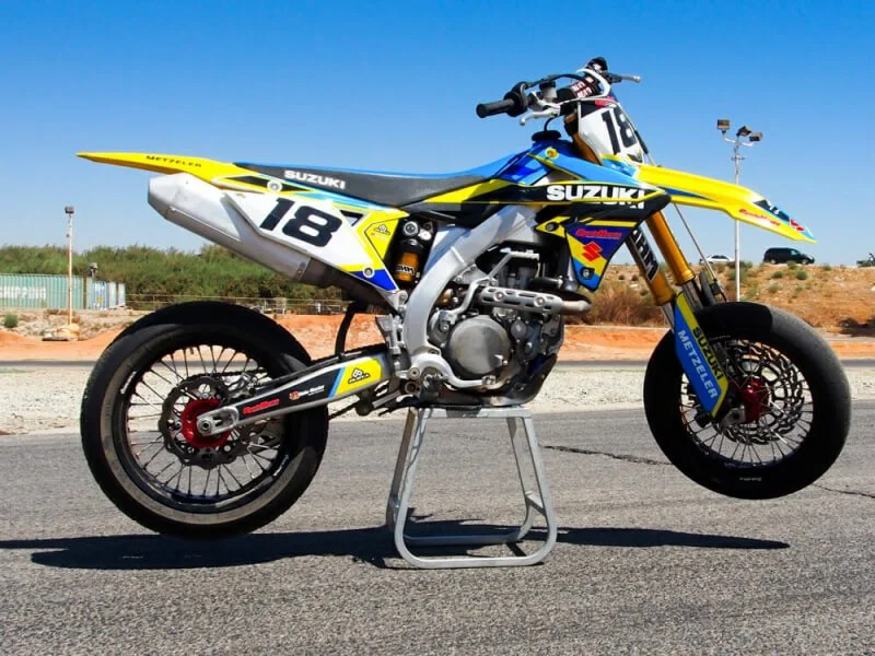 Suzuki yellow blue supermoto dirt bike with number 18 plate on motorcycle stand in outdoor setting