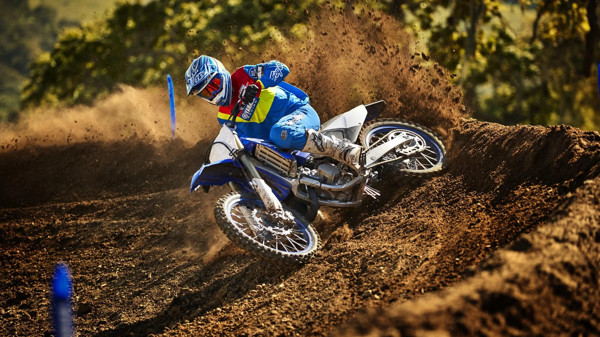 Motocross rider on lightweight blue dirt bike navigating sandy track turn, kicking up dust during competition race.