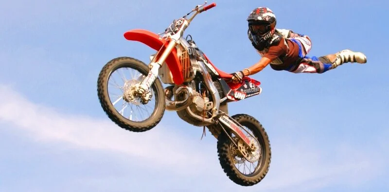 Professional dirt bike rider performing aerial backflip stunt against blue sky during extreme motocross competition