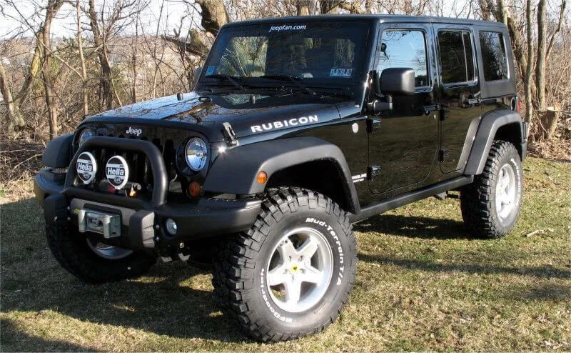 Black Jeep Wrangler Rubicon with mud tires and custom bumper parked on grass