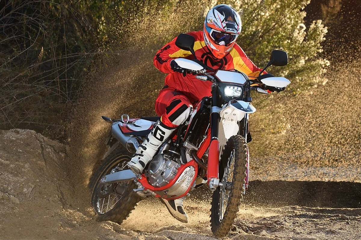 Red SWM RS 500 dual sport motorcycle with rider in action on dirt trail, kicking up dust