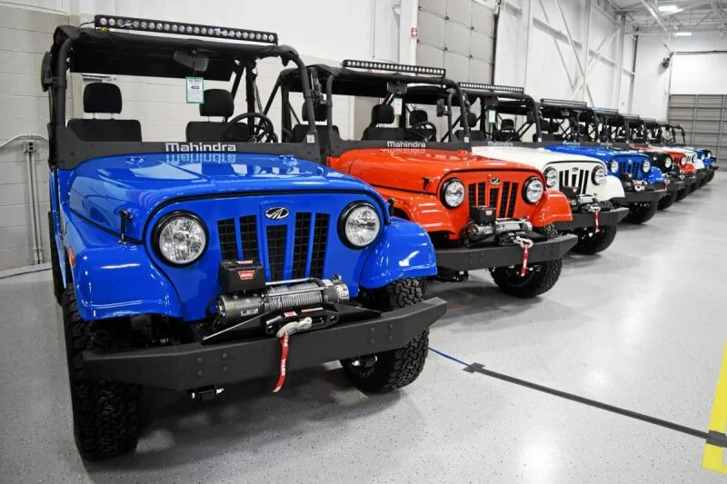 Row of Mahindra Roxor vehicles in blue and red lined up in warehouse showroom displaying in-house financing options