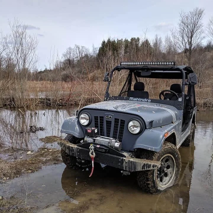 Mahindra Roxor SUV modified with roof rack stuck in muddy water during off-road adventure