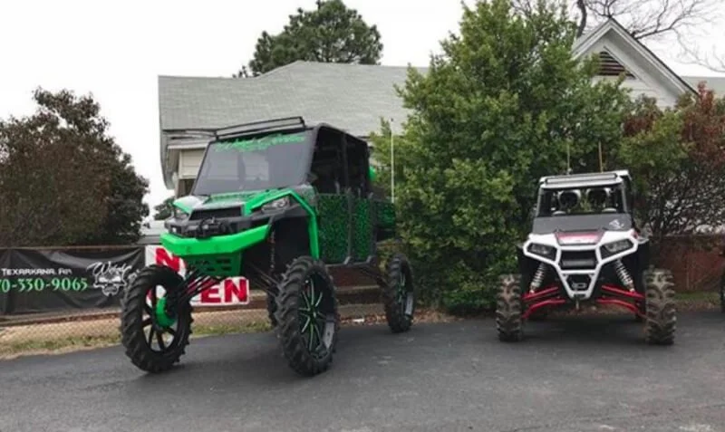 Two lifted UTVs parked in driveway, extreme suspension modifications, green and white red side-by-side vehicles