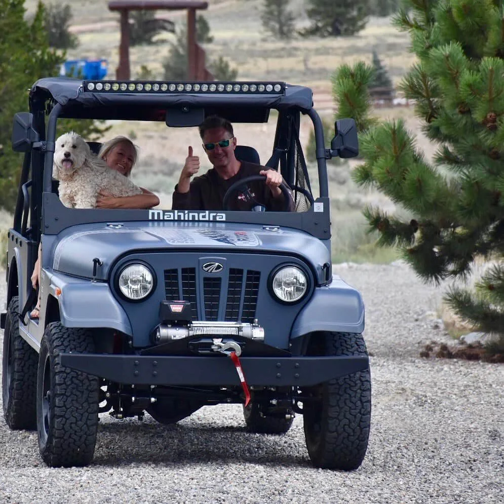 Mahindra Roxor UTV with two people and a white dog driving on gravel mountain road, thumbs up