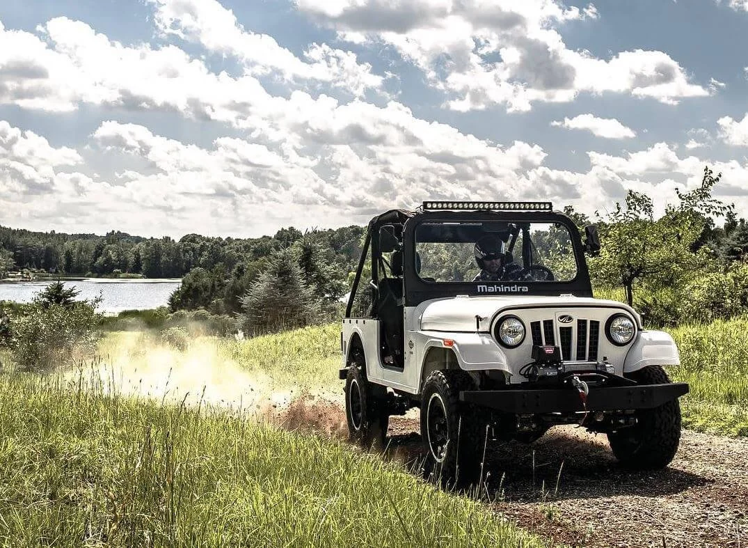 White Mahindra Roxor off-road vehicle parked on rural path with lake and forest backdrop, highlighting FCA lawsuit dispute.