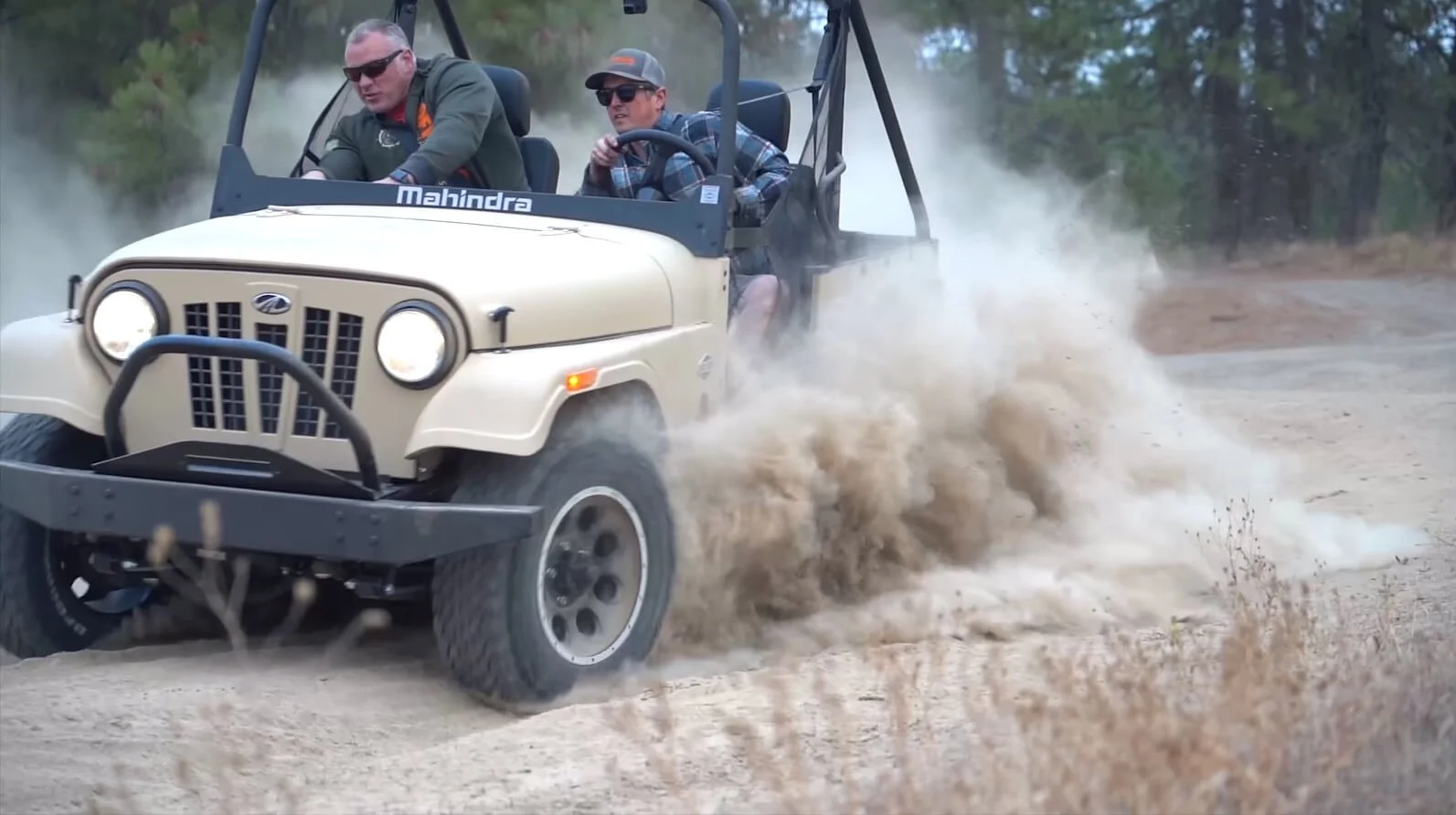 Mahindra Roxor kicking up dust on a desert trail with two passengers enjoying an off-road adventure