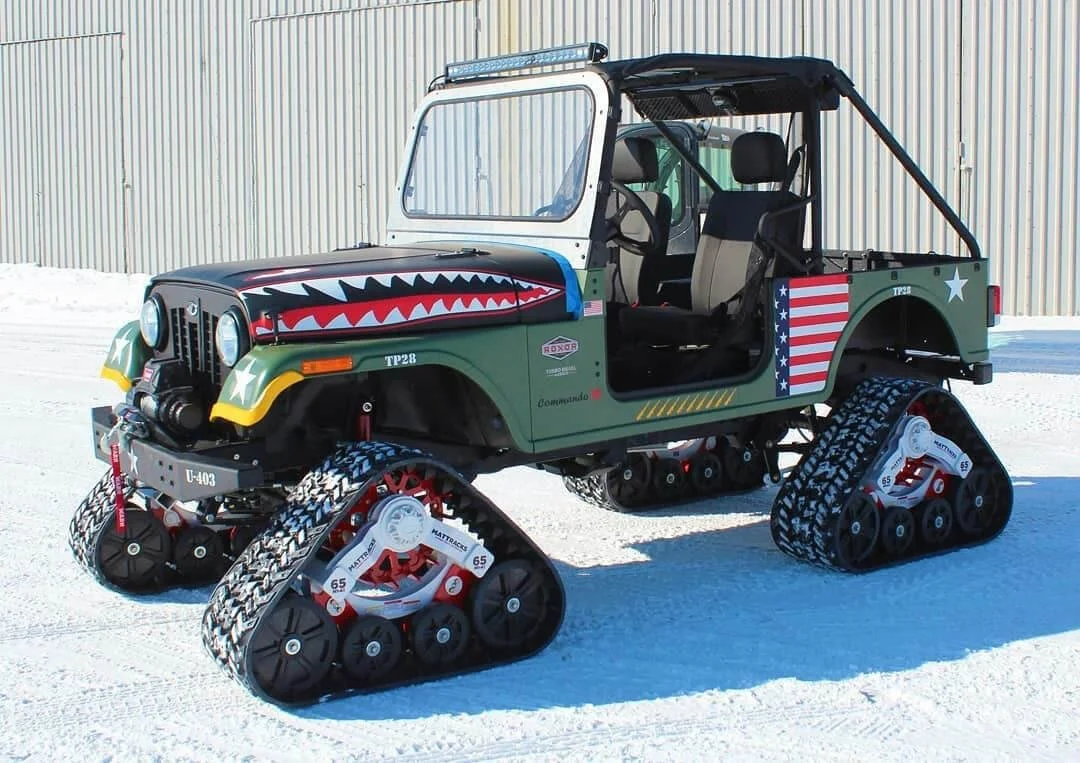 Modified Mahindra Roxor with tank treads and aggressive shark mouth graphics parked on snowy terrain for off-road adventures.