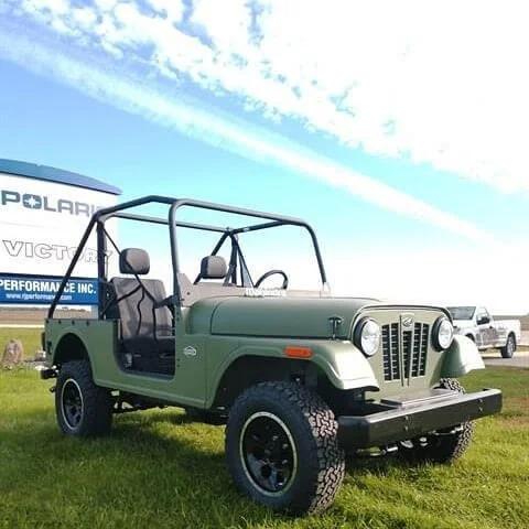Green Roxor open-air utility vehicle displayed outdoors at an event showcasing off-road capabilities and design.