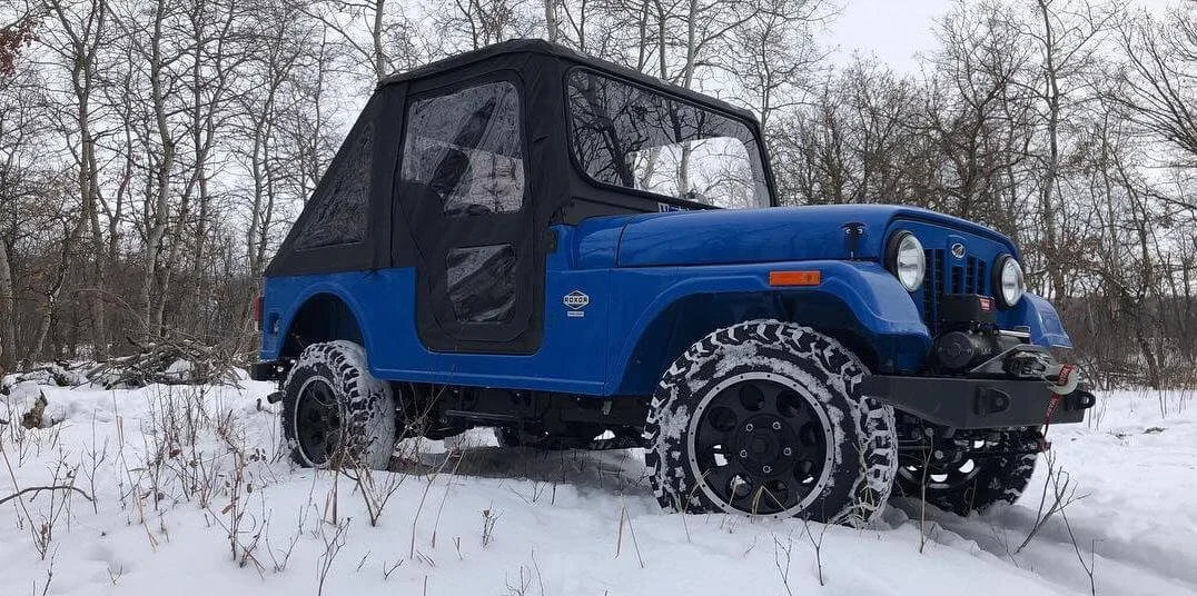 Blue Mahindra Roxor UTV with soft top parked in snowy forest, showcasing off-road capability and design
