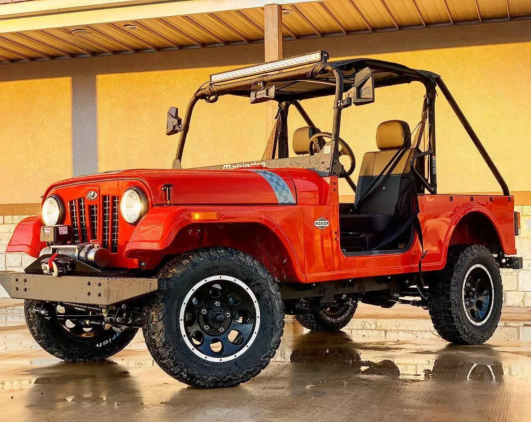 Red Mahindra Roxor utility vehicle with custom wheels and roll cage on wet concrete in covered garage setting.