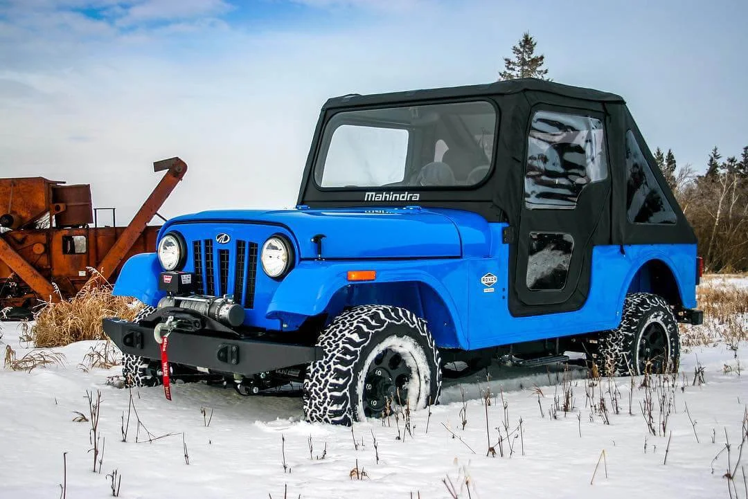 Blue Mahindra Roxor jeep with snow plow attachment parked in snowy field during winter.