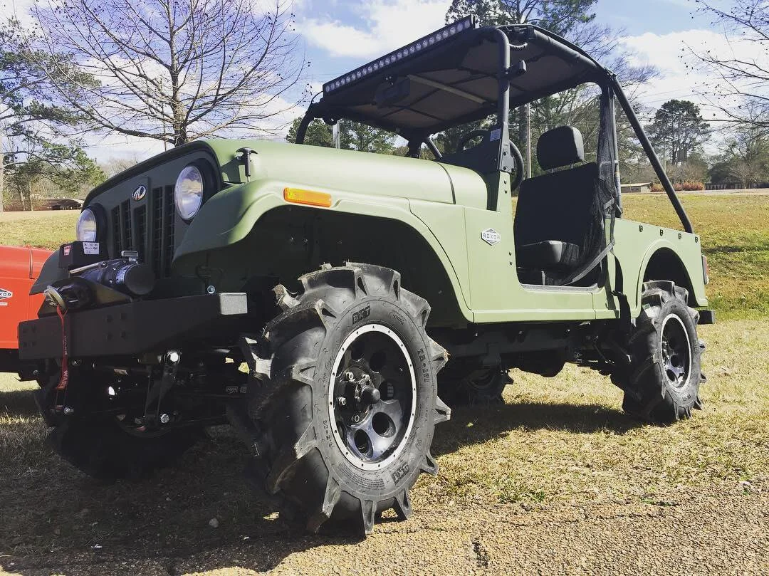 Lifted pale green Mahindra Roxor with canopy and oversized tires displayed at outdoor event on grass